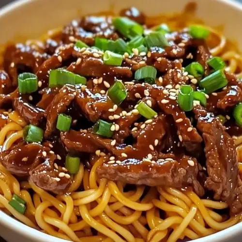 Plate of sticky beef noodles topped with sesame seeds and herbs.